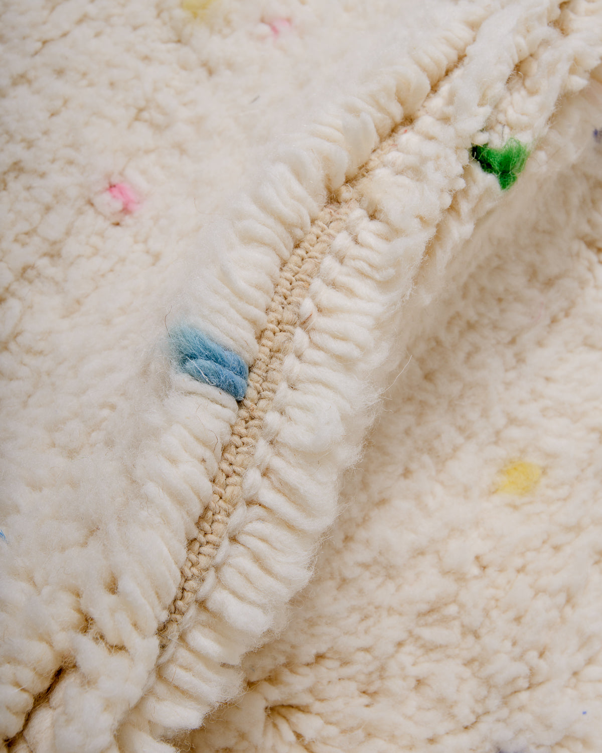 Detail of cream wool rug showing the density of the wool and the coloured strands that make up the polka dots.